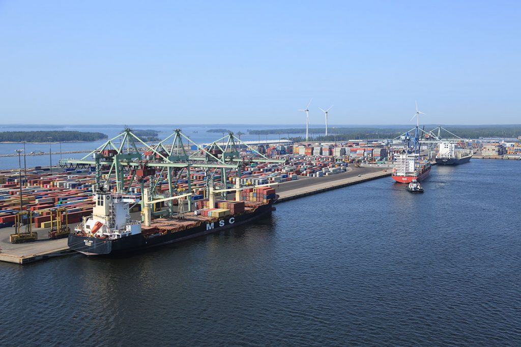 Ilmakuva satamasta, jossa on paljon merikontteja. Satamalaiturissa iso rahtialus.