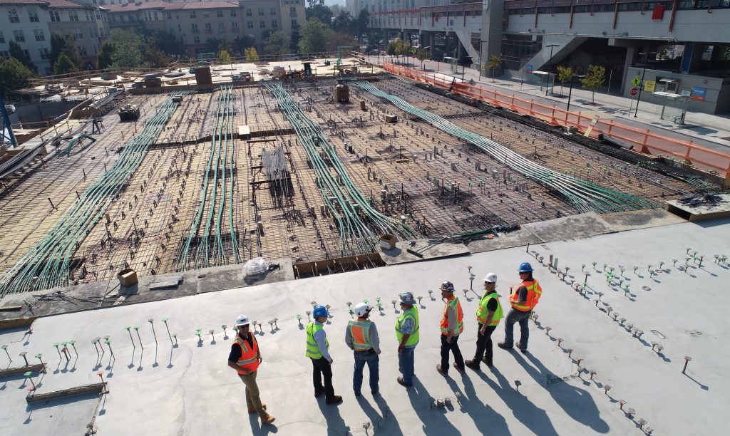 Rakennustyömaa, jossa seisoo useampi työntekijä turvakypärä päässään.